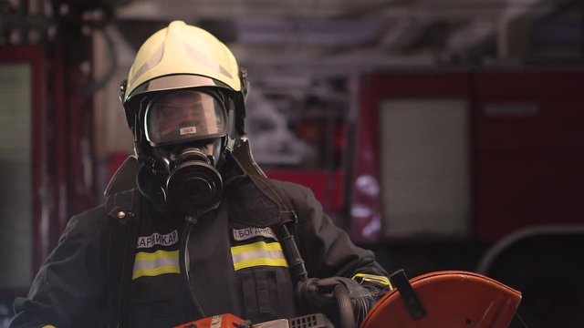 firefighter portrait wearing full equipment, oxygen mask, and power hydraulic cutting tool, smoke and fire trucks in the background. Name tag translation is fireman and model's last name.