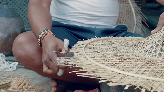 Man cutting surplus of bamboo reed on a handcrafted hat with scissors. Process of making handcrafted bamboo hat
