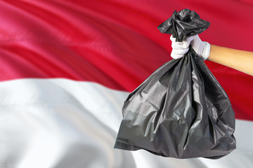 Monaco environmental protection concept. The male hand holding a garbage bag on national flag background. Ecological and recycling theme with copy space.