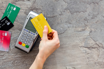 Contactless payment, paypass. Hand hold bank card near terminal on grey stone background top-down...