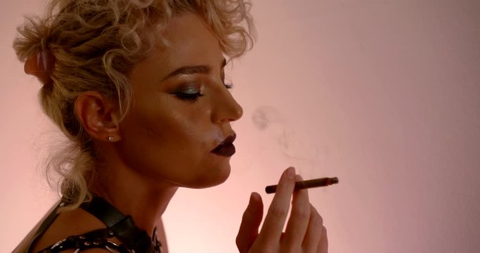 portrait of a blonde with a bright make-up in profile. she smokes a cigarette. contoured pink light. dark key