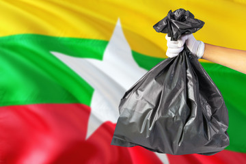 Myanmar environmental protection concept. The male hand holding a garbage bag on national flag background. Ecological and recycling theme with copy space.