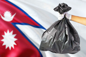 Nepal environmental protection concept. The male hand holding a garbage bag on national flag background. Ecological and recycling theme with copy space.