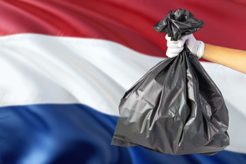 Netherlands environmental protection concept. The male hand holding a garbage bag on national flag background. Ecological and recycling theme with copy space.