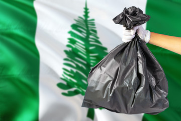 Norfolk Island environmental protection concept. The male hand holding a garbage bag on national flag background. Ecological and recycling theme with copy space.