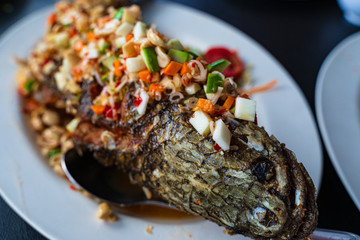 Close up soft blur focus to fried striped snake head fish with mixed herb vegetable white big dish. Thai herbs salad mixed put on top of the fish. Food thai famous menu at Thai restaurant in Thailand.