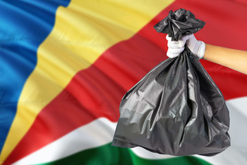 Seychelles environmental protection concept. The male hand holding a garbage bag on national flag background. Ecological and recycling theme with copy space.
