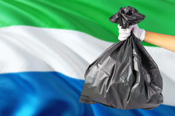 Sierra Leone environmental protection concept. The male hand holding a garbage bag on national flag background. Ecological and recycling theme with copy space.