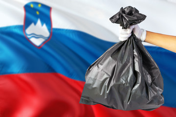 Slovenia environmental protection concept. The male hand holding a garbage bag on national flag background. Ecological and recycling theme with copy space.