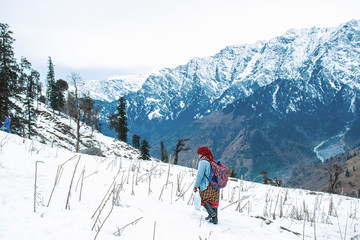 Fototapeta na wymiar Woman walking on the snow carrying bag and tea kettel to serve tourist hot tea in winter tourist season with beautiful snow mountain landscape in the background, holiday destination, kashmir, India.