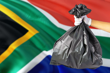 South Africa environmental protection concept. The male hand holding a garbage bag on national flag background. Ecological and recycling theme with copy space.