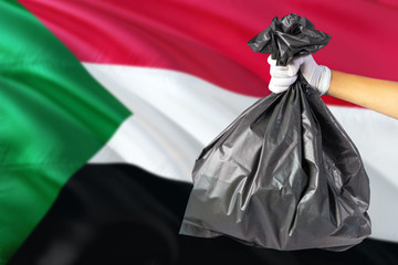 Sudan environmental protection concept. The male hand holding a garbage bag on national flag background. Ecological and recycling theme with copy space.