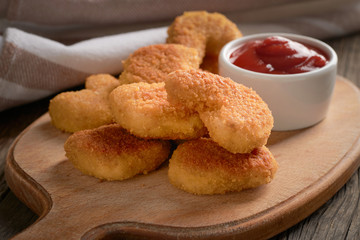Close-up of chicken nuggets in a white plate on a cutting board and chili tomato sauce on a wooden background