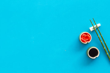 Set of chopsticks for sushi, ginger and soy sause on blue background top-down frame copy space