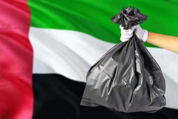 United Arab Emirates environmental protection concept. The male hand holding a garbage bag on national flag background. Ecological and recycling theme with copy space.