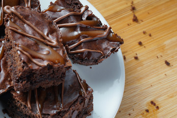 Close up of delicious dark fudgy brownies serve on round white plate ove wooden table.