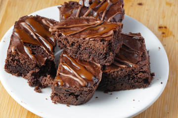 Close up of delicious dark fudgy brownies serve on round white plate ove wooden table.