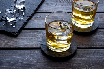 Whiskey near ice cubes on dark wooden background