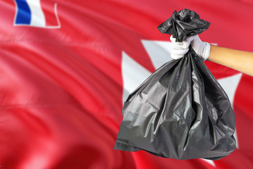 Wallis And Futuna environmental protection concept. The male hand holding a garbage bag on national flag background. Ecological and recycling theme with copy space.