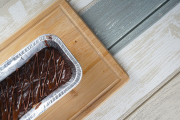 Flatlay of fresh dark chocolate brownie in foil bake pan over vintage bakground.