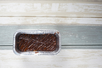 Flatlay of fresh dark chocolate brownie in foil bake pan over vintage bakground.