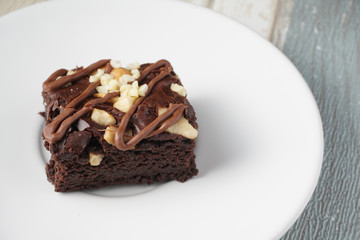 Close up on top of  moist dark chocolate brownie with mix nut on top served on white round plate over vintage background