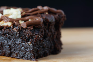 A close up of moist dark chocolate brownie with mix nut on top over wooden table.