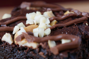 A close up of moist dark chocolate brownie with mix nut on top over wooden table.