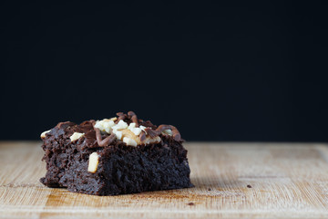 A moist dark chocolate brownie with mix nut on top over wooden table.