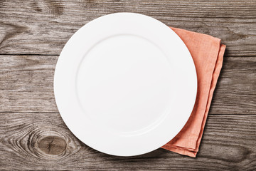 Empty plate of white color with an orange napkin on a wooden table. Food background