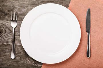 Empty ceramic plate and cutlery on a wooden table, top view. Food background