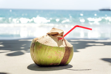 Coconut with a straw on the ocean. Tropical fruit. Coconut on white sand. Wallpaper.
