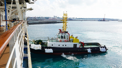A bright, powerful, new, industrial tug helps the ship maneuver in port. A tugboat helps moor a...