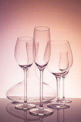 Glassware selection with wine, champagne, liquour glasses and decanter on creative background.. Fine cristal glassware concept. Vertical, warm tone