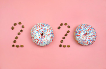 New year 2020 made of donuts and coffee beans on the pink background