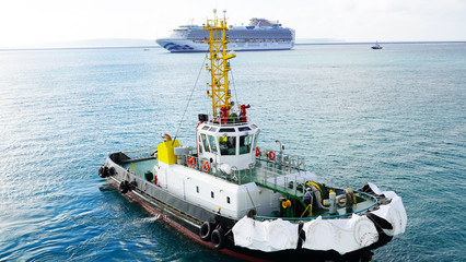 A bright, powerful, new, industrial tug helps the ship maneuver in port. A tugboat helps moor a...