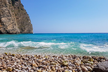 Panoramic view of pebble beach with clear azure blue water and layered rocks, beautiful mediterranean Adriatic Sea coast, Montenegro, selective focus