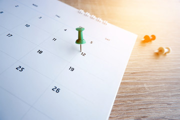 Thumbtack a date on calendar on the table with wooden background, concept for important date, meeting reminder, planning for business, travel planning concept