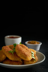 Nuggets in a plate and sauces on the backdrop on a dark background with copy space