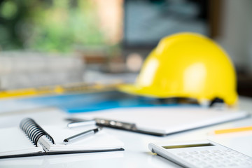 Architecture and construction concept. Empty notebook, rolls with building projects, spirit level  and architect yellow helmet on tabletop.