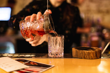 Bartender prepairing a cocktail at the bar. Pouring a drink from a mixing glass into a rocks glass. Selective focus, lifestyle.