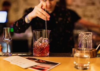 Bartender prepairing a cocktail at the bar. Stirring a drink in the mixing glass with a bar spoon. Selective focus, lifestyle.