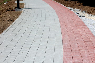 Grey and light red stone tiles sidewalk at local public park surrounded with gravel and dry soil on warm sunny summer day