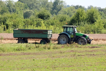 Green and black farm tractor with connected rusted vintage old tractor trailer left in local field...