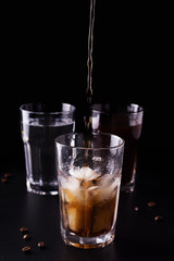 coffee is poured into a glass with ice. refreshing drink on a black background