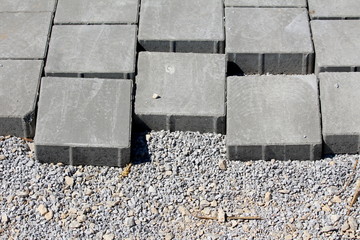 Installation of rectangle grey and light red stone tiles on gravel at local construction site on warm sunny summer day