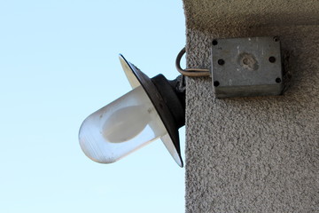 Old style outdoor white bulb enclosed in glass protection surrounded with metal reflective surface mounted on family house corner next to electrical junction box