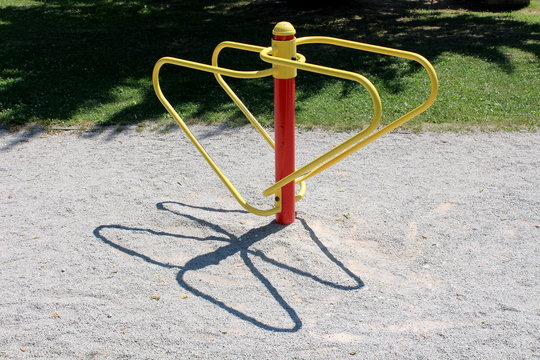 Parallel rails colorful red and yellow public park fitness outdoor exercise equipment with two different heights surrounded with gravel and freshly cut grass in local public park