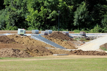 Public sidewalk under construction with piles of stone tiles prepared for installation next to intermediate bulk container or IBC plastic tank with metal cage and concrete steps