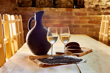 Two glasses of white wine, grape seeds, a clay jug and a few pieces of bread on a wooden table in a restaurant